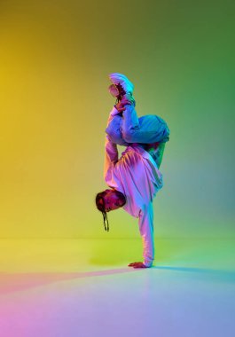 Dehşet saçı olan, hip-hop dansı yapan genç yetenekli bir adam. Gradyan, yeşil stüdyo arka planında neon ışıklarıyla breakdance yapıyor. Sokak dansı konsepti, moda, gençlik, hobi, dinamik, reklam
