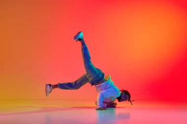 Dans gösterisi. Renkli turuncu arka planda neon ışıkta break dans yapan genç adamın dinamik görüntüsü. Sokak dansı konsepti, moda, gençlik, hobi, dinamik, reklam