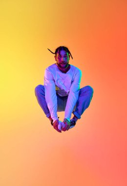 Bir atlayışta. Dehşet dansı yapan sokak stili genç bir adam. Neon ışıklarıyla arka plandaki turuncu renkli stüdyoya karşı breakdance yapıyor. Sokak dansı konsepti, moda, gençlik, hobi, dinamik, reklam