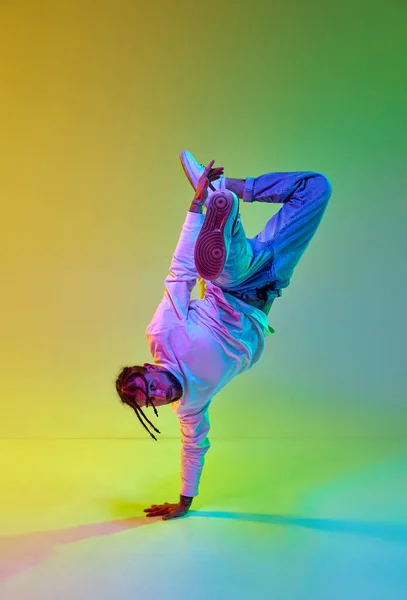 stock image Young sportive guy with dreads hairstyle dancing hip-hop, breakdance against gradient yellow green studio background in neon light. Concept of street style dance, fashion, youth, hobby, dynamics, ad