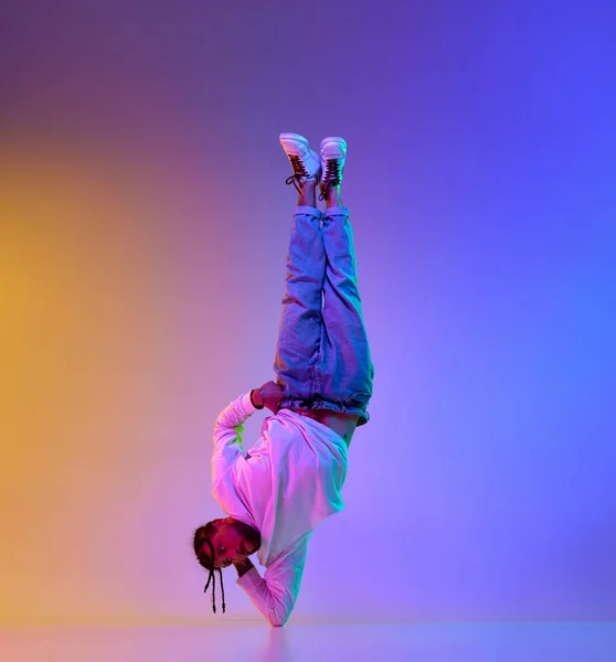 stock image Young sportive guy with dreads hairstyle dancing hip-hop, breakdance against gradient multicolored studio background in neon light. Concept of street style dance, fashion, youth, hobby, dynamics, ad