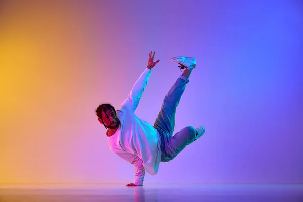 stock image Dance show. Young guy dancing contemp, breakdance and hip-hop against gradient multicolored studio background in neon light. Concept of street style dance, fashion, youth, hobby, dynamics, ad