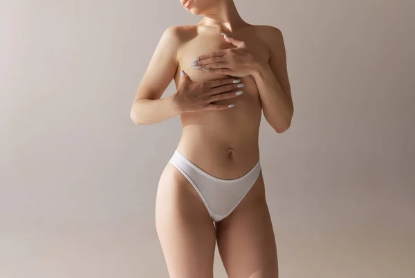 手で乳房を覆うスリムなボディの若い女性のトリミングされた画像 グレーのスタジオ背景に下着姿のモデル マンモプラスチック 自然の美しさ 女性らしさの概念 — ストック写真