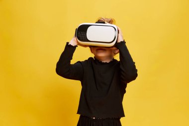 Küçük bir kızın portresi, sarı stüdyo arka planında VR gözlükleriyle duran bir çocuk. Eğitim, eğlence, oyun. Çocukluk kavramı, duygular, yaşam tarzı, moda, neşe. Ad