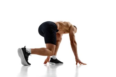 Hazır, hazır, başla. Kaslı bir adam, profesyonel bir atlet, koşucu beyaz stüdyo geçmişine karşı yarışacak pozisyonda. Spor, rekabet, sağlık, güç ve hız kavramı, reklam