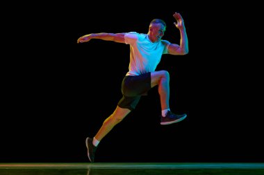 Genç adamın dinamik görüntüsü kaslı, güçlü, formda, profesyonel koşucu neon ışıkta siyah stüdyonun arka planına karşı. Spor, rekabet, sağlık, güç ve hız kavramı, reklam