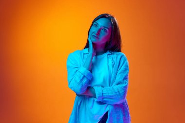 Şefkatli, sakin, gündelik giysiler içindeki genç bir kadının portresi. Renkli turuncu arka planda, neon ışıkta, rüya gibi bir bakışla duruyor. Gençlik kavramı, insani duygular, yaşam tarzı, reklam