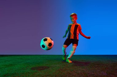 Aktif, enerjik okul çağındaki çocuk, futbol oyuncusu eğitimi neon renkli koyu mavi arka planda. Çocuk eğitimi kavramı, hobiler, beceriler, rekabet, başarı
