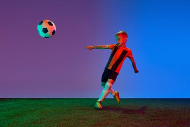 Sportif bir çocuk, kırmızı üniformalı bir çocuk neon ışıkta futbol antrenmanı yapıyor. Eylem kavramı, spor yaşam tarzı, takım oyunu, sağlık, enerji, canlılık ve reklam