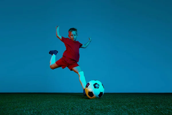 stock image Male beginner soccer player in sports uniform in action, motion with ball over dark blue background in neon. Concept of action, sportive lifestyle, team game, health, energy, vitality and ad