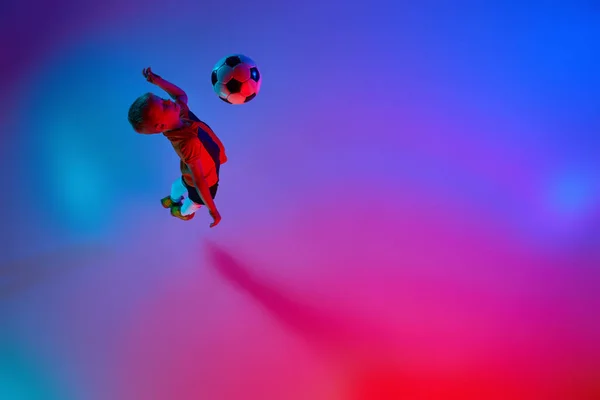 グラデーションの赤青ネオンでサッカーボールでトレーニング中に小さな男の子を再生する空中ビュー アクションの概念 スポーツライフスタイル チームゲーム エネルギー 活力と広告 — ストック写真