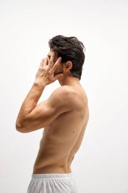 Baş ağrısı. Beyaz atölyenin arka planında beyaz gömleksiz genç bir adamın profiline dokun. Erkek sağlığı kavramı, erkek vücudu güzelliği, ilaç, reklam
