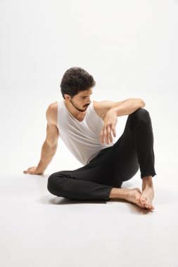 Ev kıyafetleri giyen kaslı erkek manken, beyaz arka planda izole bir şekilde yerde oturuyor. Erkeklik. Erkek sağlığı, güzellik, vücut ve cilt bakımı, fitness ve reklam kavramı.