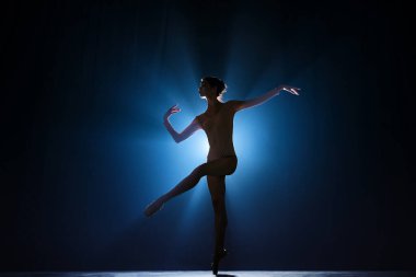 Çekici, sanatsal, yetenekli genç kız, klasik dans eden balerin, spot ışıklarıyla koyu mavi arka plana karşı gösteri. Sanat konsepti, klasik bale, yaratıcılık, koreografi, güzellik
