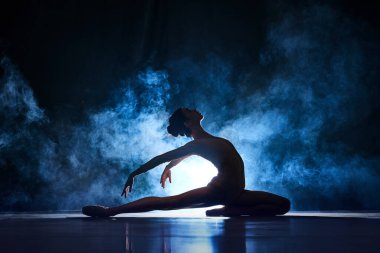 Zarif, güzel, zarif genç bir kadın, dumanlı spot ışıklarıyla koyu mavi arka planda dans eden balerin. Sanat konsepti, klasik bale, yaratıcılık, koreografi, güzellik, reklam