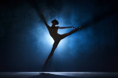 İnce, güzel, zarif balerin sahne ışıklarıyla koyu mavi arka plana karşı yaratıcı bir performans sergiliyor. Sanat konsepti, klasik bale, yaratıcılık, koreografi, güzellik, reklam