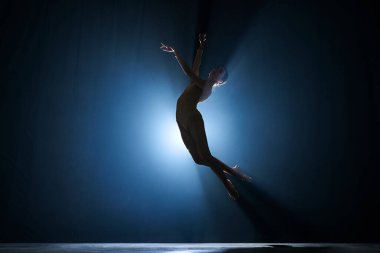 İnce, güzel, zarif balerin sahne ışıklarıyla koyu mavi arka plana karşı yaratıcı bir performans sergiliyor. Sanat konsepti, klasik bale, yaratıcılık, koreografi, güzellik, reklam