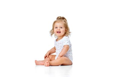 Güzel, mutlu, gülümseyen bir çocuk. Küçük bir kız bebek, beyaz stüdyo arka planında neşe ve eğlence içinde yerde oturuyor. Çocukluk kavramı, annelik, bakım, hayat, doğum. İlan için alanı kopyala