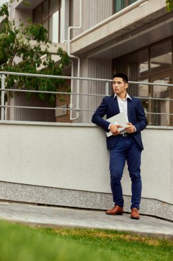 Yakışıklı genç adamın portresi, mavi takım elbiseli ofis müdürü dışarıda tabletle duruyor. Konsantrasyon ve motivasyon. İş kavramı, kariyer gelişimi, modern ofis, profesyonel meslek