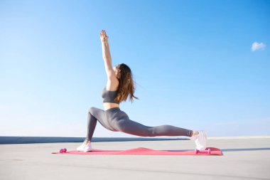 Genç, esnek, spor giyimli, rahat bir kadın, esneme egzersizleri yapıyor, güneşli bir günde açık havada antrenman yapıyor. Spor anlayışı, aktif ve sağlıklı yaşam tarzı, güzellik, fitness, reklam