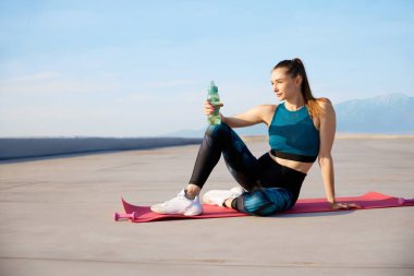 Sıvı kaybı. Güneşli bir günde açık havada antrenman yaptıktan sonra şık, rahat spor taytları ve spor ayakkabıları giyen genç ve güzel bir kadın. Spor anlayışı, sağlıklı yaşam tarzı, güzellik, fitness, reklam