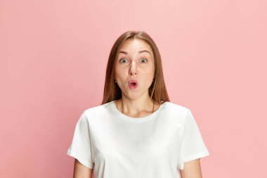Gayri resmi beyaz tişörtlü güzel bir kadının portresi pembe stüdyo arka planına karşı şok olmuş bir yüz ifadesi. Ne hoş bir sürpriz. İnsan duyguları kavramı, yaşam tarzı, gençlik, moda, reklam