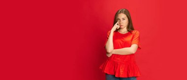 Babamın yanında duran genç bir kadının portresi, gücenmiş, sıkılmış bir yüz ve kırmızı stüdyo arka planına bakan bir kamera. İnsan duyguları kavramı, yaşam tarzı, gençlik, moda, reklam