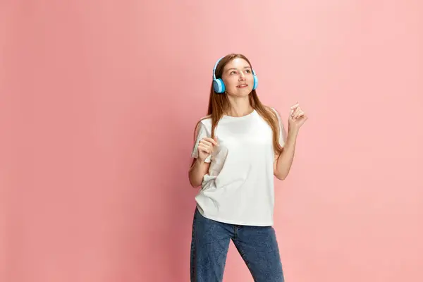 ピンクのスタジオの背景に対してヘッドフォンで音楽を聴くカジュアルな服の若い美しい少女の肖像画 人間の感情 ライフスタイル ファッション 美しさ 広告の概念 — ストック写真