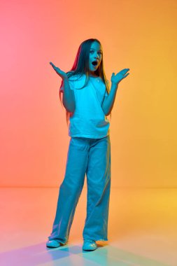 Vay canına. Sevimli okul çağındaki kızın portresi, neon ışıklı arka planda günlük tarz kıyafetler giyen bir çocuk. Çocukluk kavramı, duygular, çocuk modası. Model şaşırmış görünüyor.