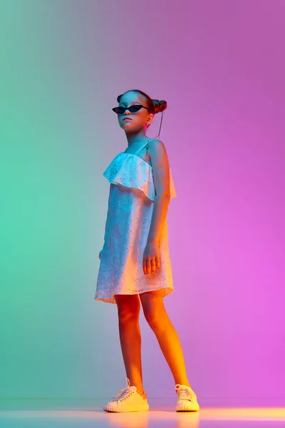 stock image Fashionable little girl, child wearing sunglasses posing over neon light background. Concept of childhood, emotions, kids fashion. Model looks delighted