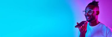 Afrika kökenli Afrikalı bir adam elinde telefonla neon rengi mavi-pembe bir arka plandan sesleniyor. Nesil kavramı, yaşam tarzı, iletişim, teknolojiler, kopyalanma alanı, reklam