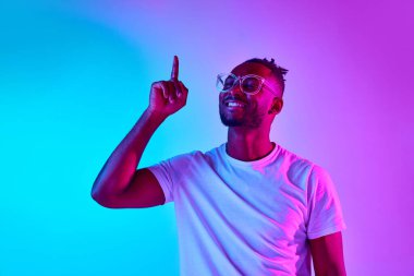 Harika bir fikir. Gözlüklü, gülümseyen Afro-Amerikan bir adamın neon renkli arka plan üzerinde parmağını kaldırdığı bir fotoğraf. Duyguların kavramı, düşünceler, iş dünyası, reklam,