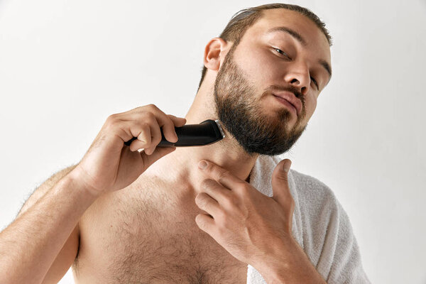 Close up shoot of man looking at camera with towel on shoulder shaving his face with razor isolated over gray background. Concept of beauty, appearance, facecare, health, youth and ad..