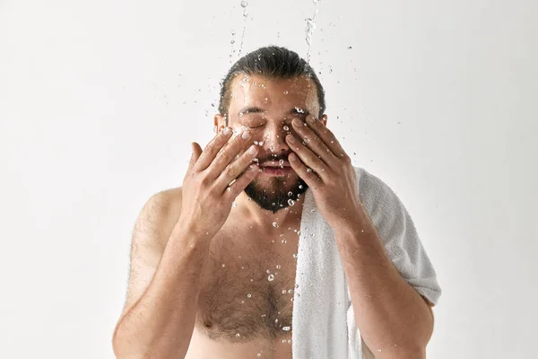 Hygiene. Morning routine. Photoshoot of man washing face with water splash over light grey background. Concept of beauty, appearance, facecare, health youth and ad.