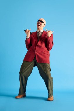Tam uzunluk görüntüsü. Bıyıklı, iş elbisesi giymiş, mavi arka planda bağıran ve sevinen kel bir adam. Duyguların kavramı, başarı, bağbozumu, retro ve reklam