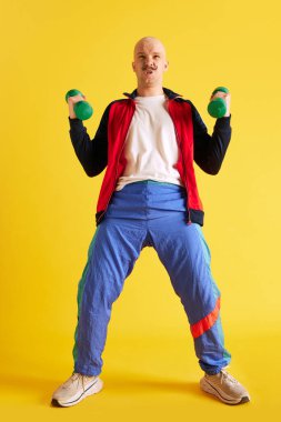 Spor giyinmiş bir adamın dikey vücut çekimi sarı arka plan üzerinde dambıllar olan kaslar giyer. Spor anlayışı, sağlıklı yaşam tarzı, eğitim ve reklam.