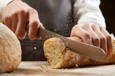 Tahta masada mutfak bıçağıyla taze çıtır ekmekleri kesen adama yaklaş. Sağlıklı yeme, beslenme ve el işi ürünü kavramı.