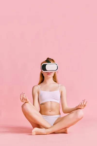 Sportive young girl practicing yoga in lotus pose in VR headset glasses. Concept of sport, health and virtual reality.
