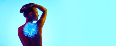 Pankart. Arkadan bak. Dijital neon projektör ışıkları olan genç ve güzel bir kadın. Cyan arka planda çiçekler gösteriyor. Dijital sanat, moda, fütürizm. Reklam için boşluk kopyala. Pankart