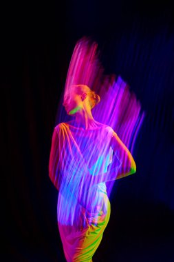 Beyaz Midi elbiseli, pembe ve mor neon ışıklarla poz veren, siyah mod arka planına uzun süre maruz kalan bir kadın. Duyguların kavramı, güzellik, yüz ifadesi, gençlik, arzu.