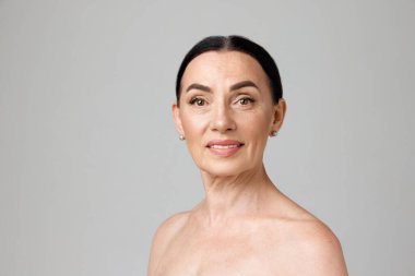 Gri arka planda kameraya bakan çıplak omuzlu, güzel, koyu renk saçlı bir kadının portresi. Moda, güzellik, kaplıca, kozmetoloji, cilt bakımı, kadınlık kavramı.