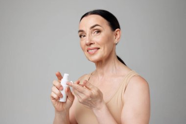 Neşeli, orta yaşlı bir kadın boş kozmetik ürünleri şişesi kullanıyor. Moda, güzellik, kaplıca, kozmetoloji, cilt bakımı ve sağlık konsepti.