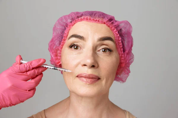 Smoothing out wrinkles.Portrait of elder woman doing beauty injection. Hands in pink gloves hold a syringe. Face lift. Beauty, cosmetology, anti-aging, skin care, injections concept.