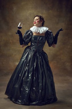 Çöp poşetlerinden yapılmış siyah elbiseli zarif bir kadın elinde şarap kadehiyle klasik arka planda poz veriyor. Aristokrat kadın portresi. Çevre sorunları, geri dönüşüm, tarz, moda kavramı.