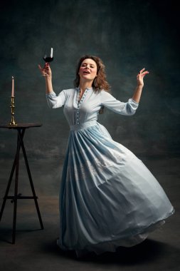 Şarap ve mutluluk. Mavi tarihi elbise giyen ve bir bardak şarapla dans eden aristokrat bir kadının tam boy portresi. Sağlıklı yaşam tarzı, diyet, tarz, moda kavramı.