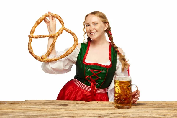 若い女の子のウェイトレスは 伝統的なバイエルンやドイツのディルンドルを着て 巨大なプレッツェルでビールマグを提供しています オクトーバーフェスト 飲み物 食べ物のコンセプト Adのためのスペースをコピーする — ストック写真