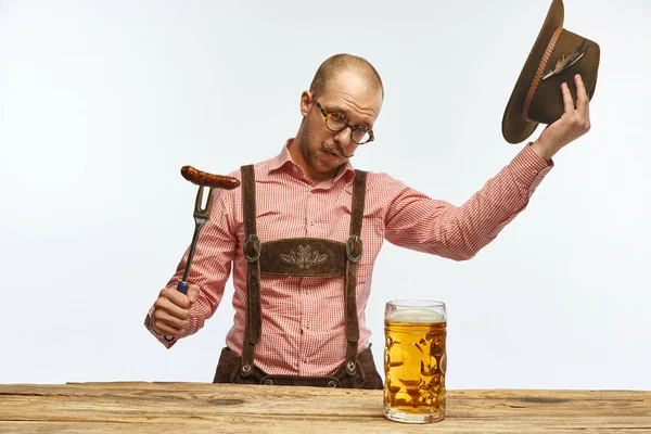 尊敬する 白い背景に隔離された巨大なグラスビールと伝統的なドイツの衣装を身に着けている帽子を持つ1人の若い男性 アルコール オクトーバーフェストの概念 Adのためのスペースをコピーする — ストック写真