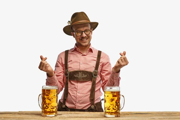 I love beer festival. Happy man with mustaches wearing traditional german outfit with beer showing heart symbol shape feelings. Concept of Oktoberfest, traditions, drinks and food. Copy space for ad