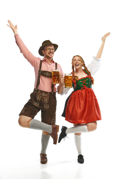 Two dancing friends. Full lenght portrait of emotional man and woman wearing folk festival outfits with Bavarian beer glasses. Concept of alcohol, traditions, holidays, festival. Copy space for ad