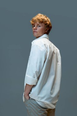 Gri arka planda kameraya bakarken beyaz gömlekli, ciddi kırmızı ve kıvırcık saçlı bir adamın portresi. Doğal güzellik kavramı, moda, kendine dikkat, erkeklik. Ad